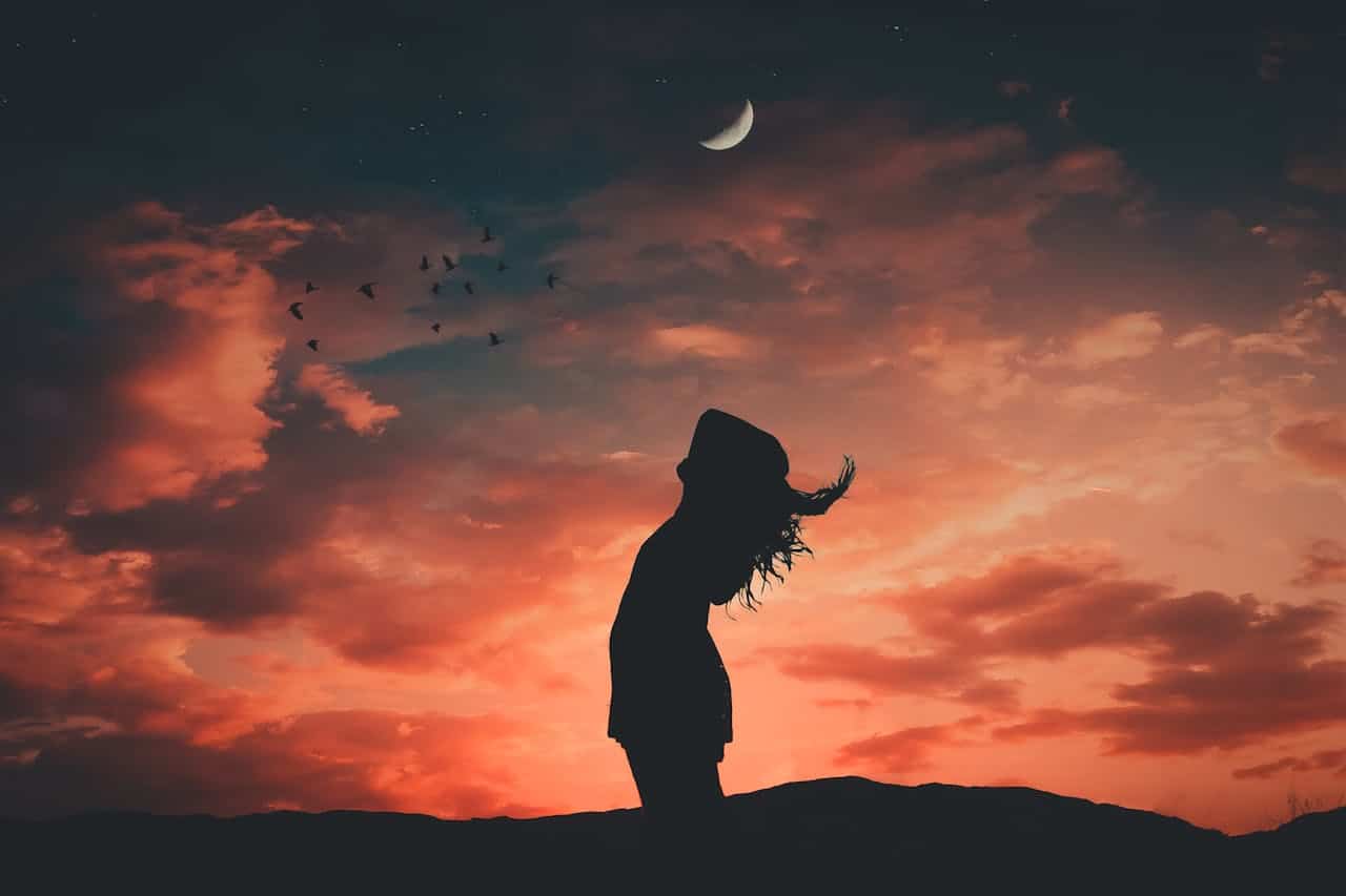 Silhouette of a woman standing against a sunset sky with a crescent moon, symbolizing reflection and emotional overwhelm