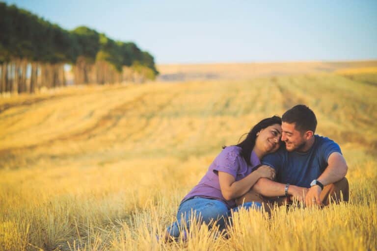 Couple sitting closely together in a sunny field, showing emotional connection and warmth.