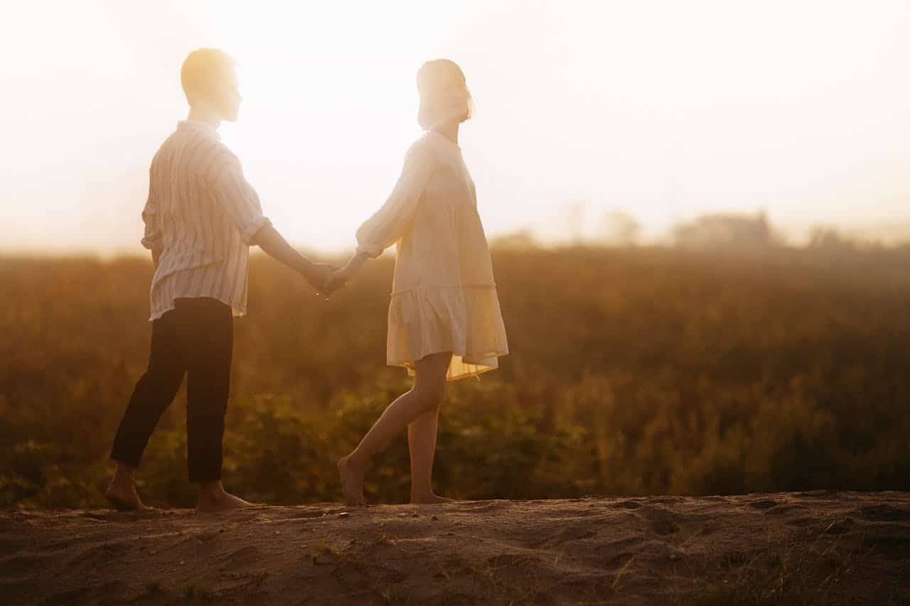 Couple holding hands outdoors during sunset, symbolizing support and togetherness.